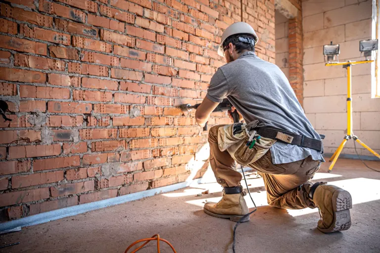 Trabajador agujereando pared de ladrillo.