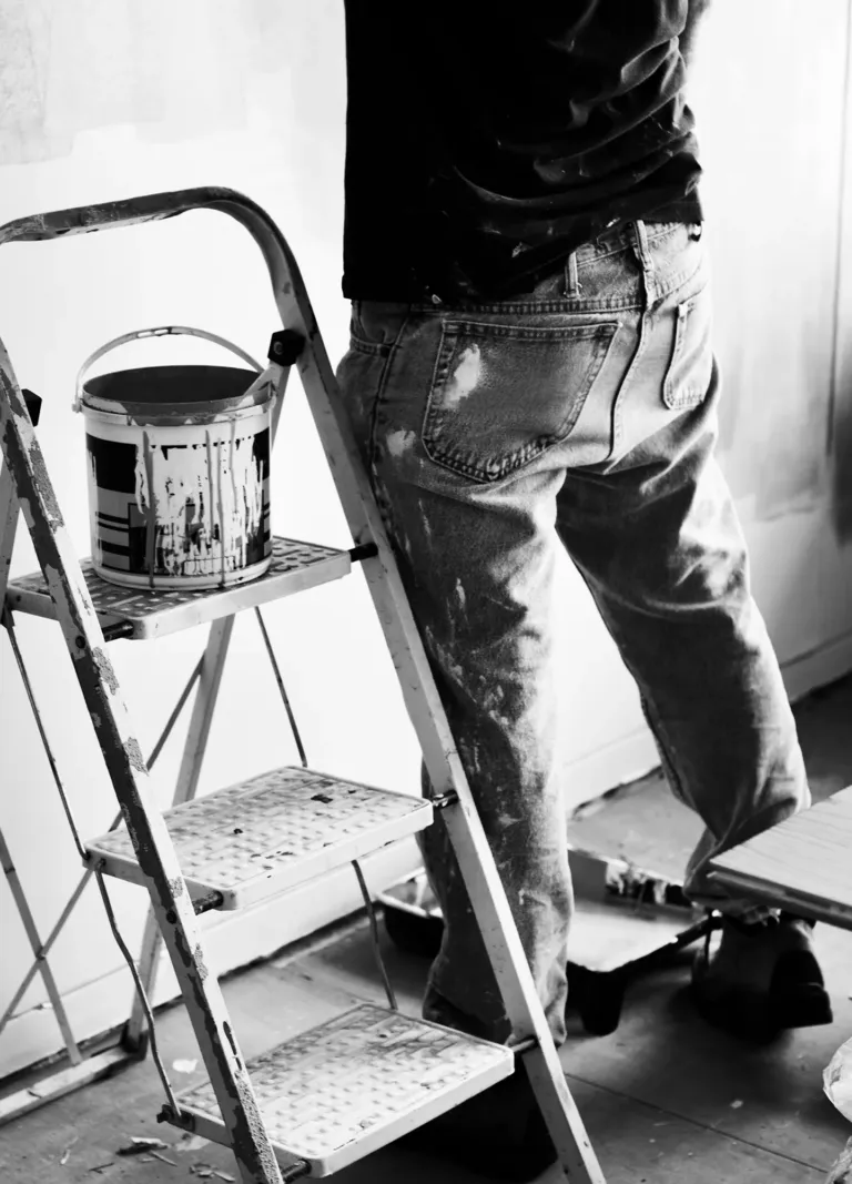 Pintor con cubo de pintura sobre escalera.